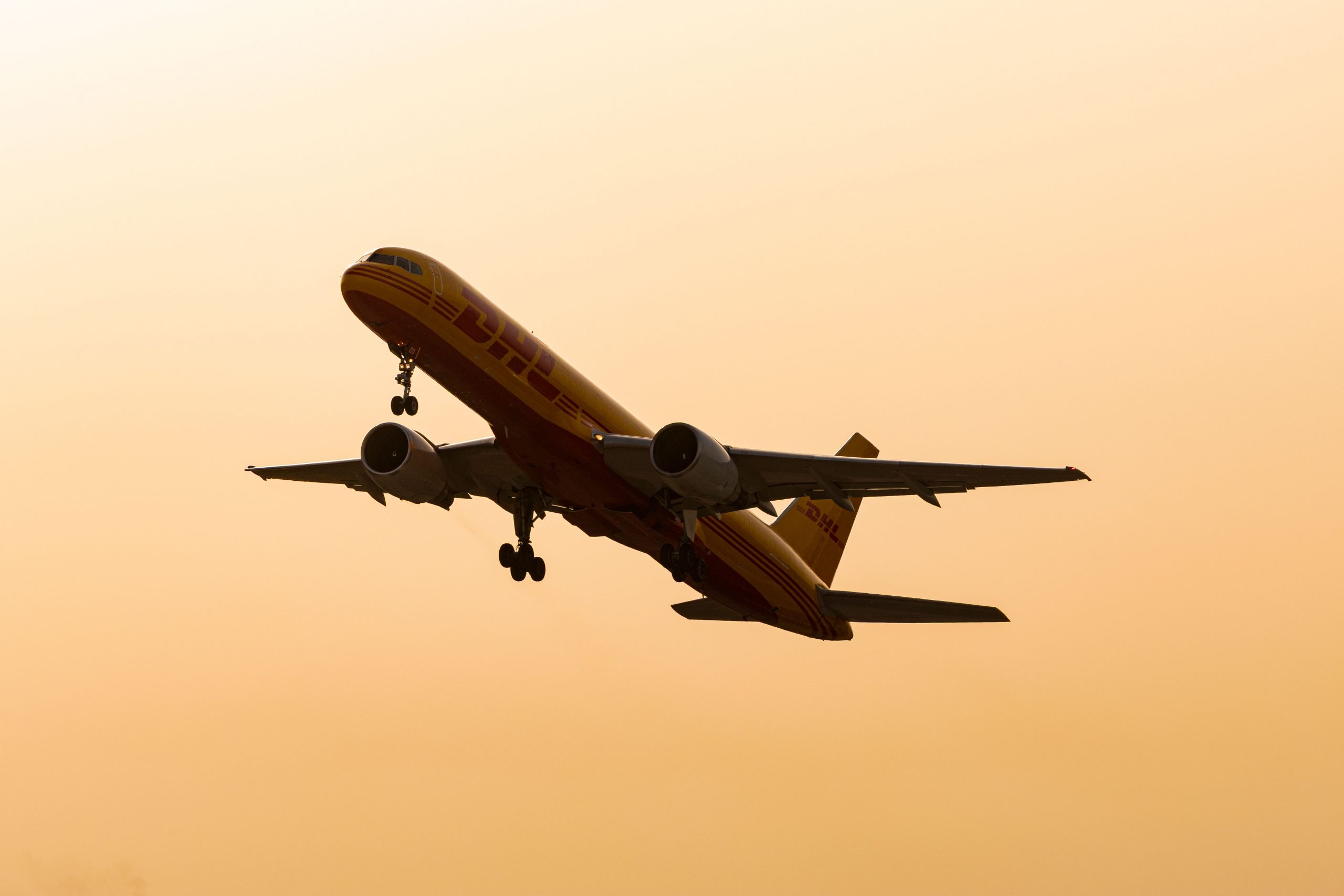 Cargo airplane flying in silhouette against a warm sunset sky.