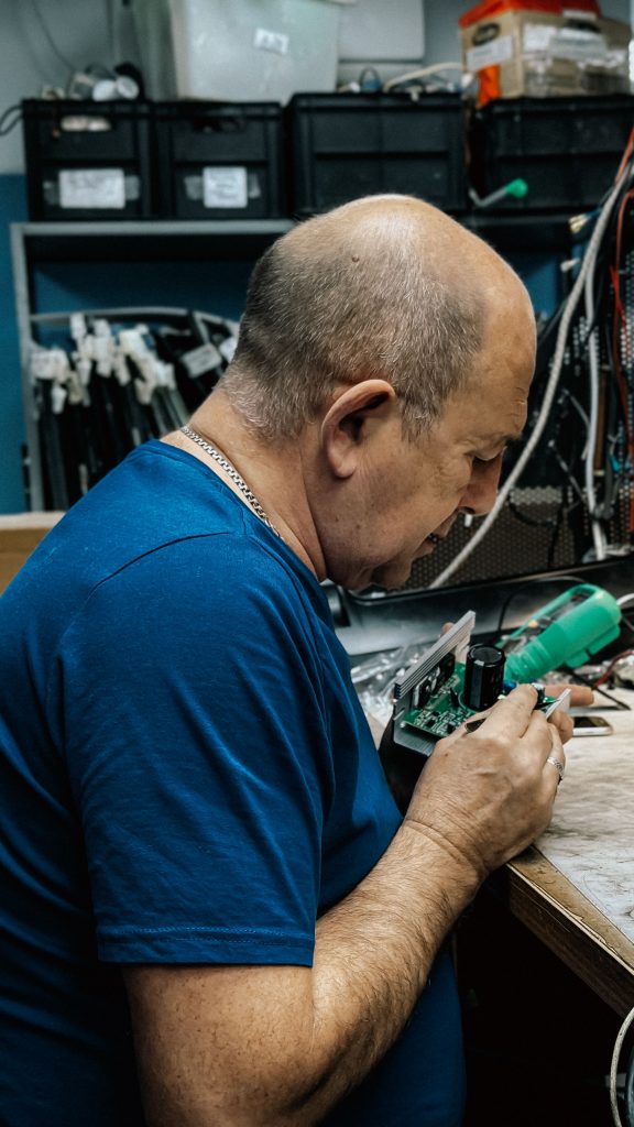 Skilled technician working meticulously on electronics in workshop. Tools and cables visible.