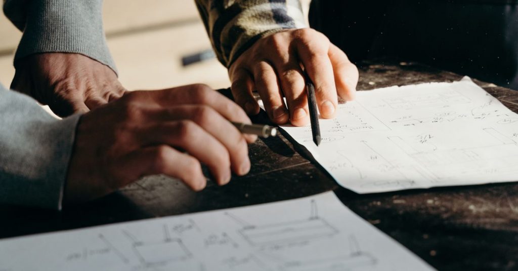 Close-up of hands working on blueprints in a workshop environment.